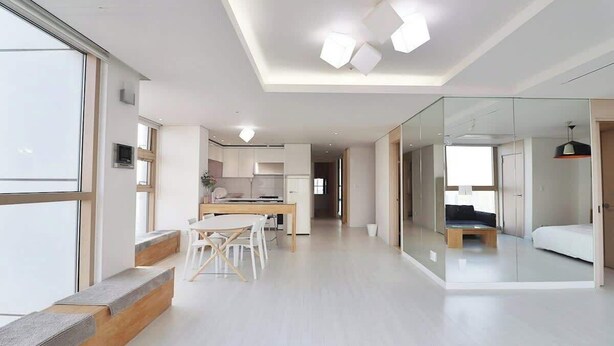 Un interno moderno con zona pranzo, cucina e camera da letto separata da una parete di vetro.