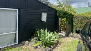 Eine schwarze Gartenhütte mit einer weißen Garagentür, einem an der Wand montierten Verteilerkasten und einem geparkten Fahrzeug in der Nähe.