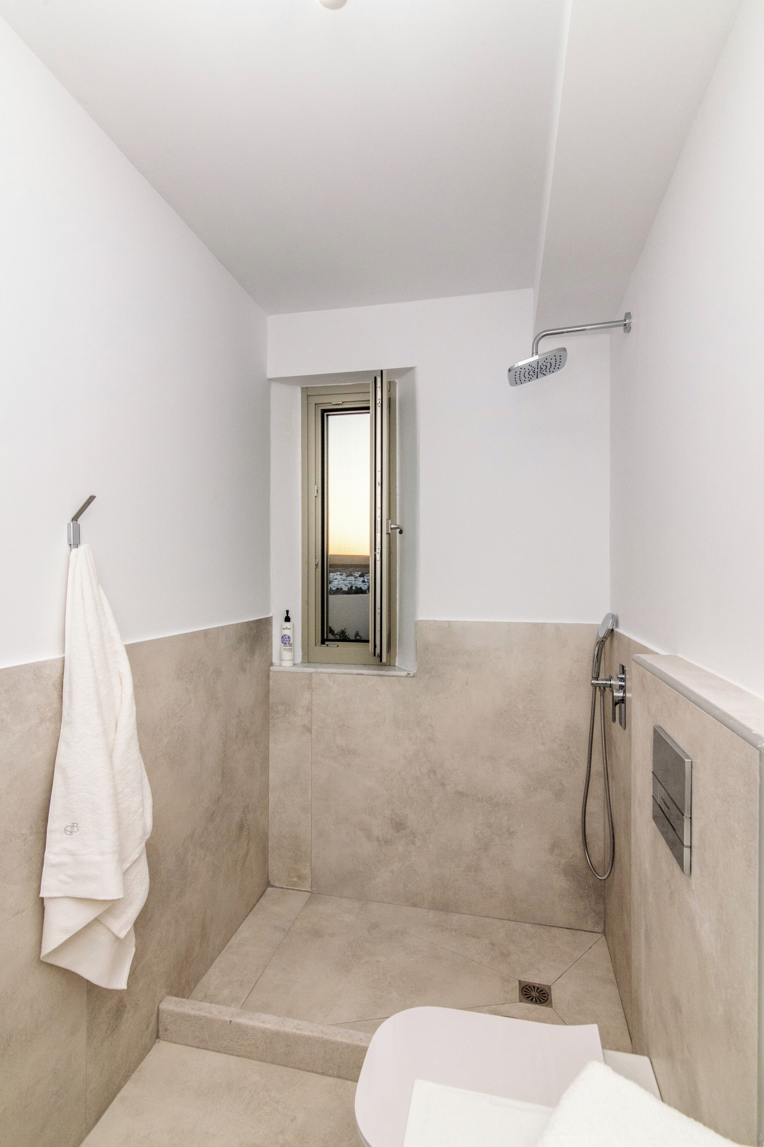 A small, modern bathroom with a shower, a towel rack, and a window.