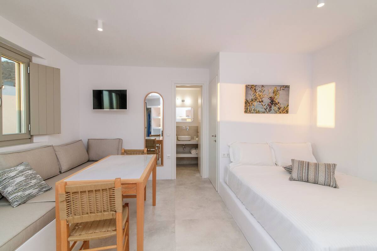 A modern, well-lit room with a sofa, a dining table, and a TV mounted on the wall.