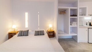 A modern hotel room with a large bed, two bedside lamps, a built-in wardrobe, and a small kitchenette. - Blu Dot Tinos by TinosHost (Tinos)