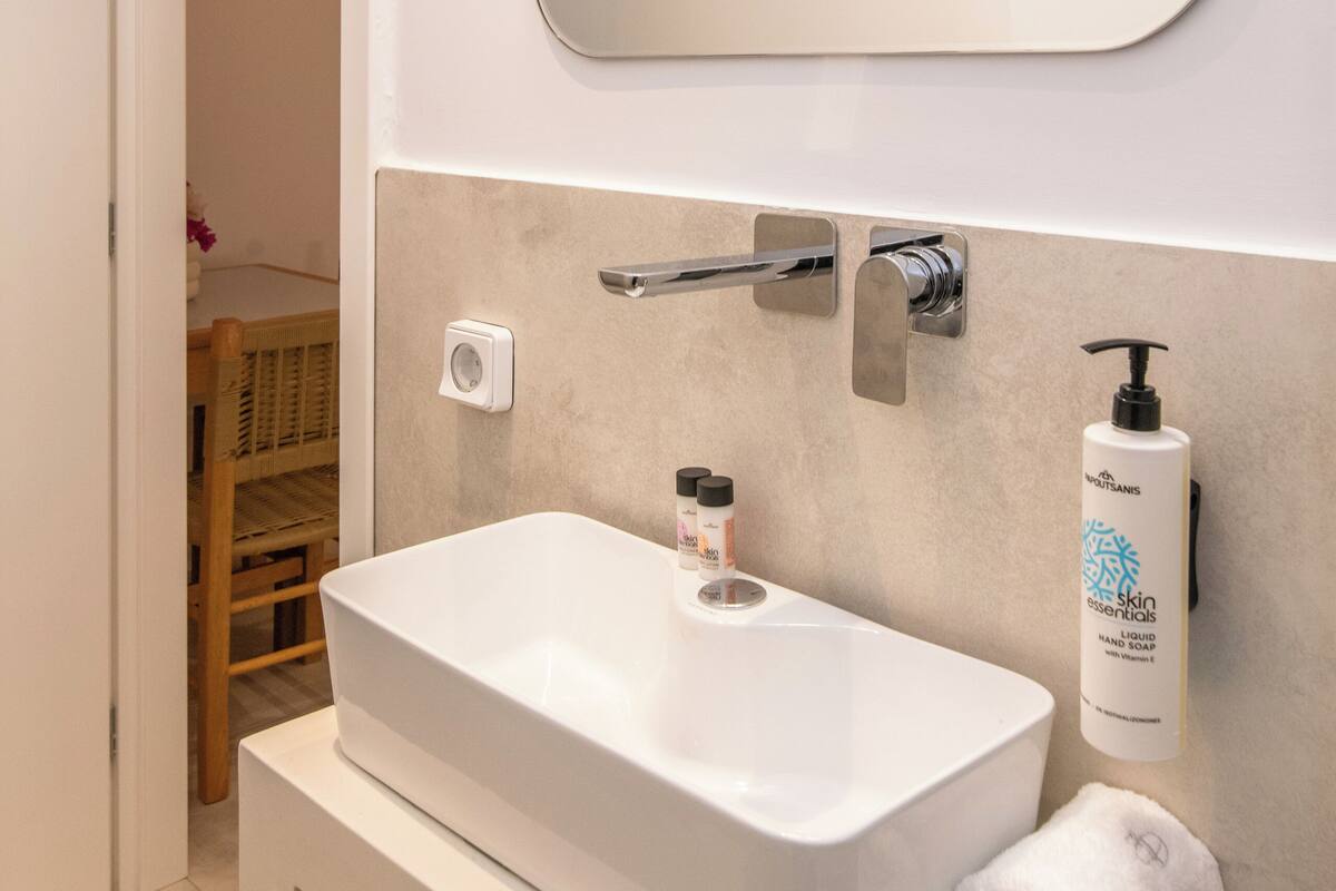 A bathroom with a white sink, a mirror, and a hand soap dispenser.