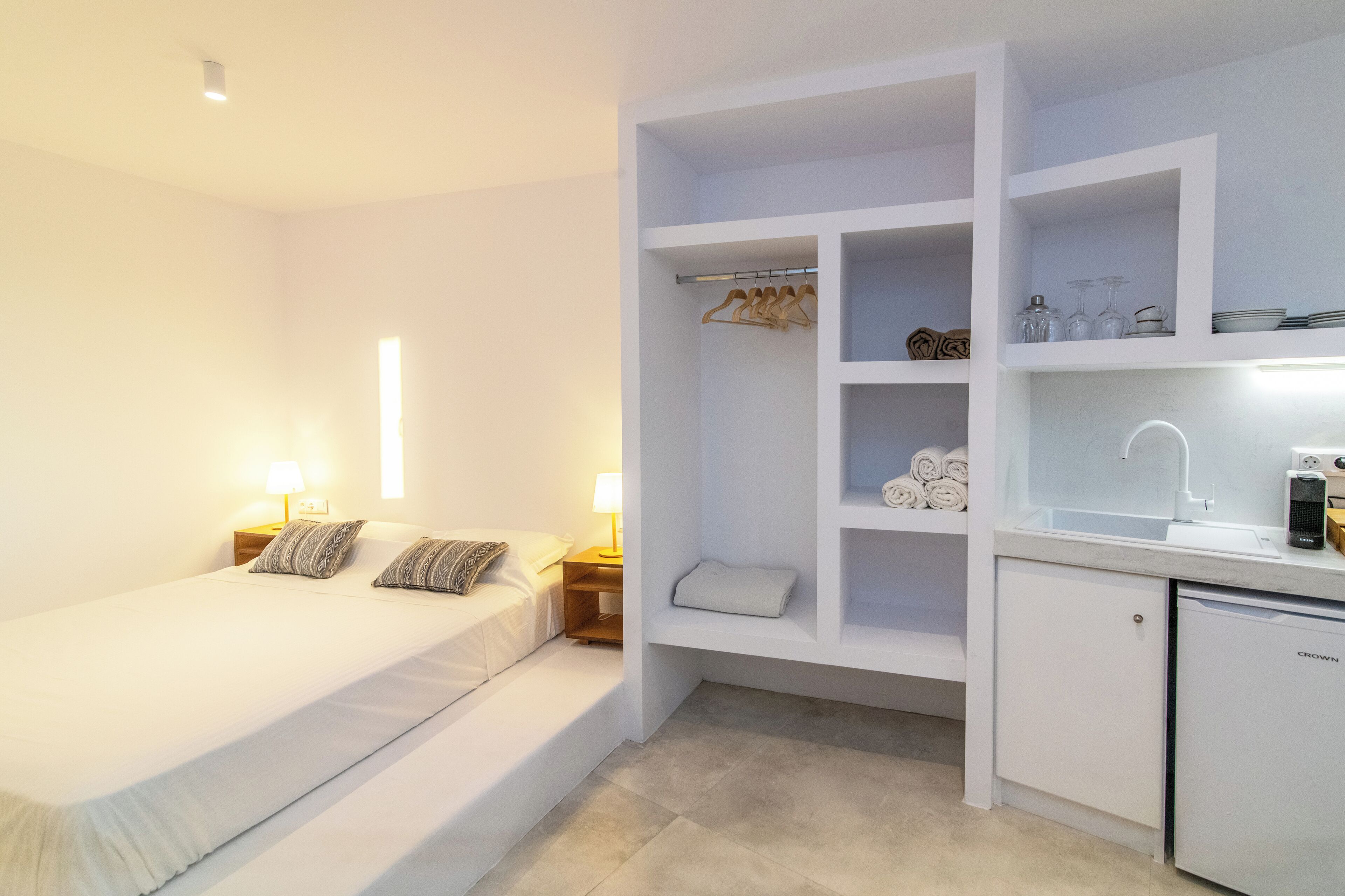 Een slaapkamer met een bed, nachtkastjes en een inbouwkast met planken.
