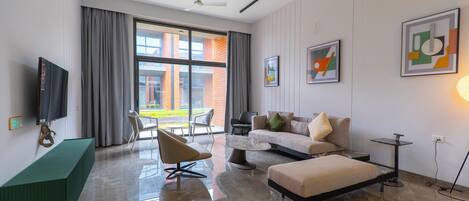 Un salon moderne avec un canapé, un pouf et des fauteuils, un téléviseur à écran plat et des œuvres d’art accrochées aux murs.