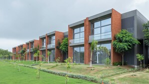 A modern building with multiple floors, large windows, and a well-maintained garden with various plants. - Swajan Bankers Community (Padra)