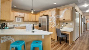 Une cuisine moderne avec des meubles en bois, un îlot central doté de tabourets, un réfrigérateur et un luminaire suspendu.