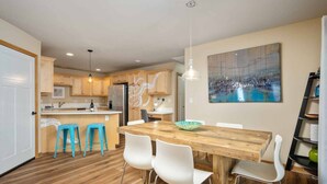 Une cuisine moderne avec des meubles en bois, un îlot central et un coin repas comprenant une table en bois et des chaises blanches.