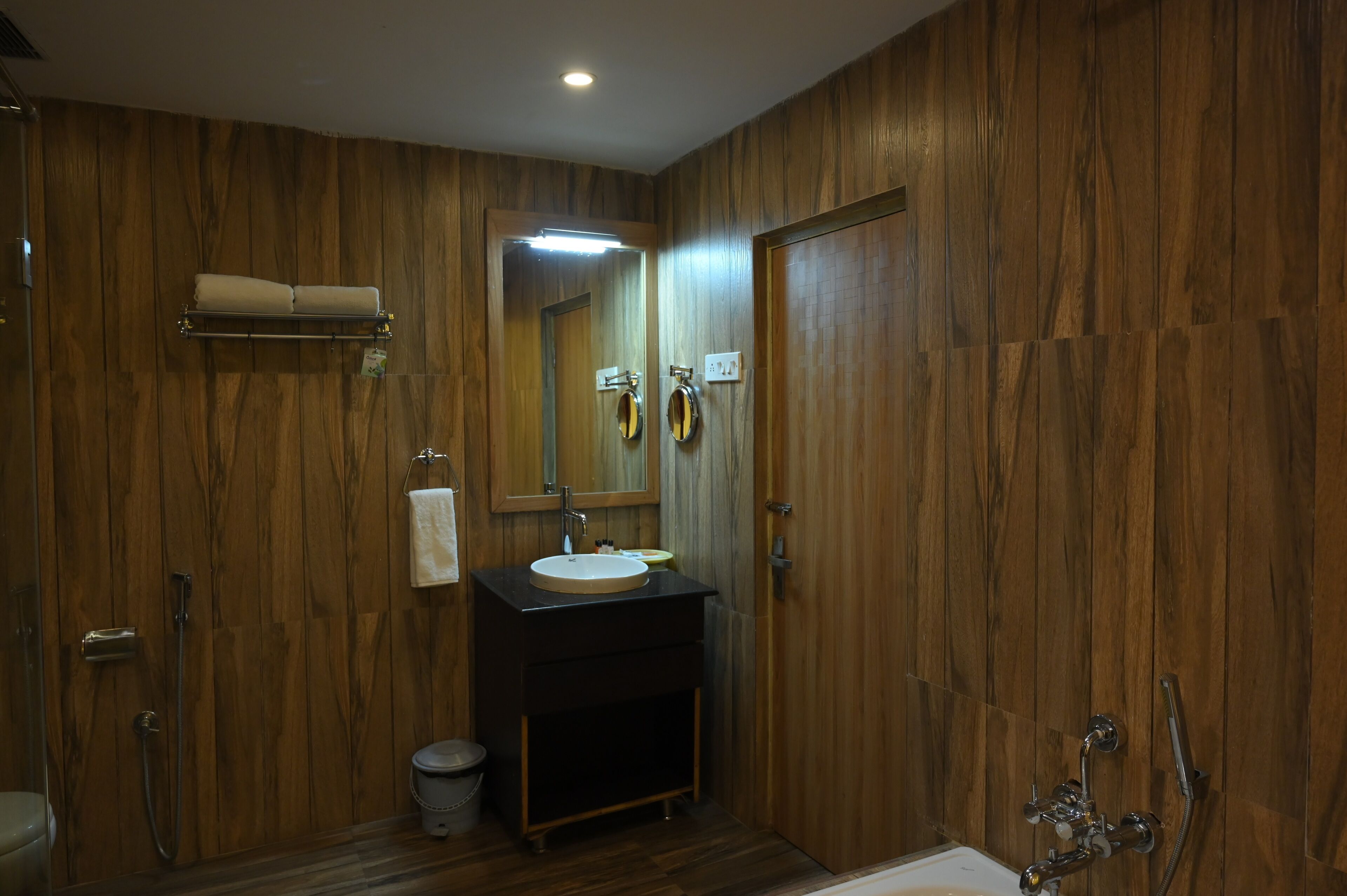 A wooden-paneled bathroom with a sink, mirror, towel rack, and shower.