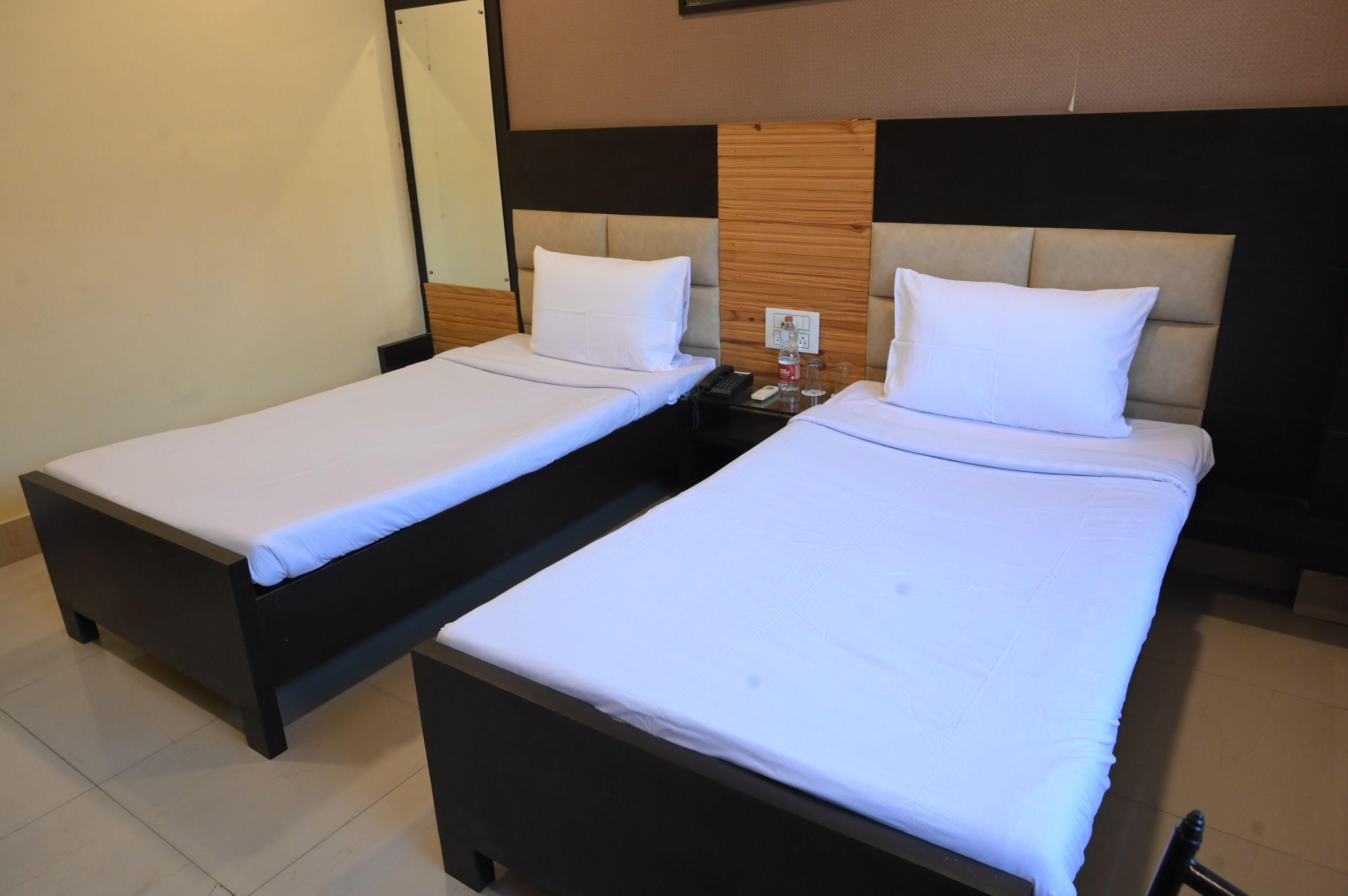 Two single beds with white linens, a bedside table with a phone and a glass, and a wall-mounted mirror.
