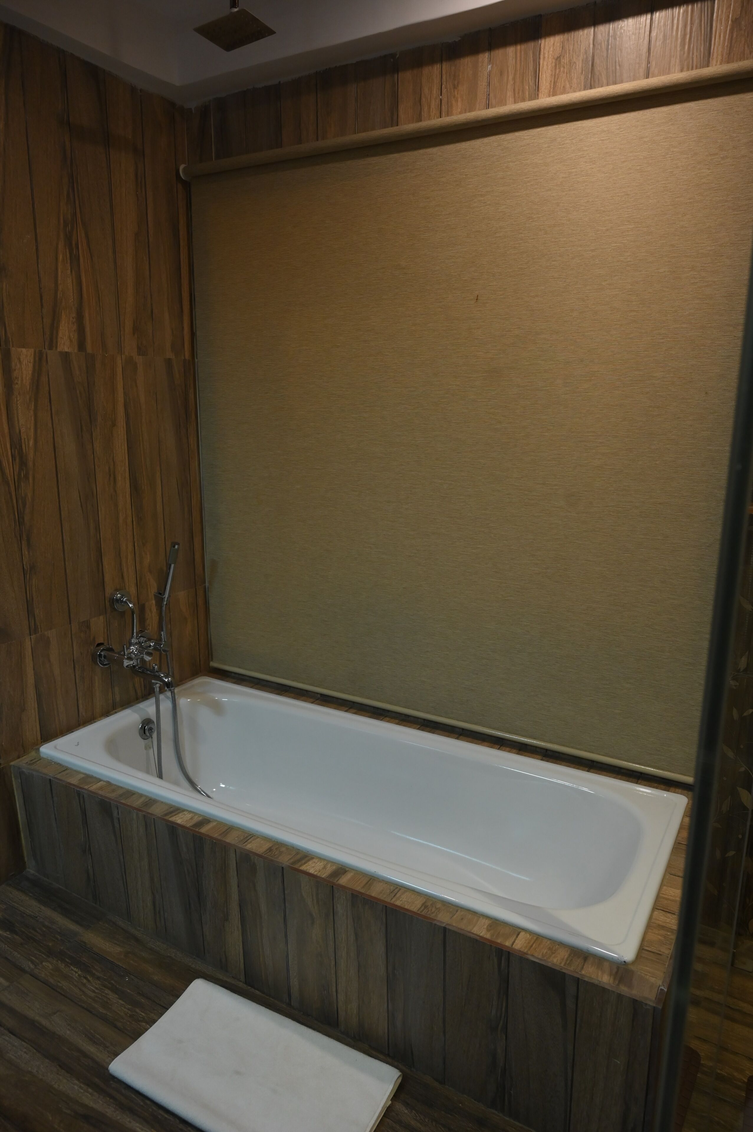 A modern bathroom with a wooden panel wall, a white bathtub, and a small white bench.