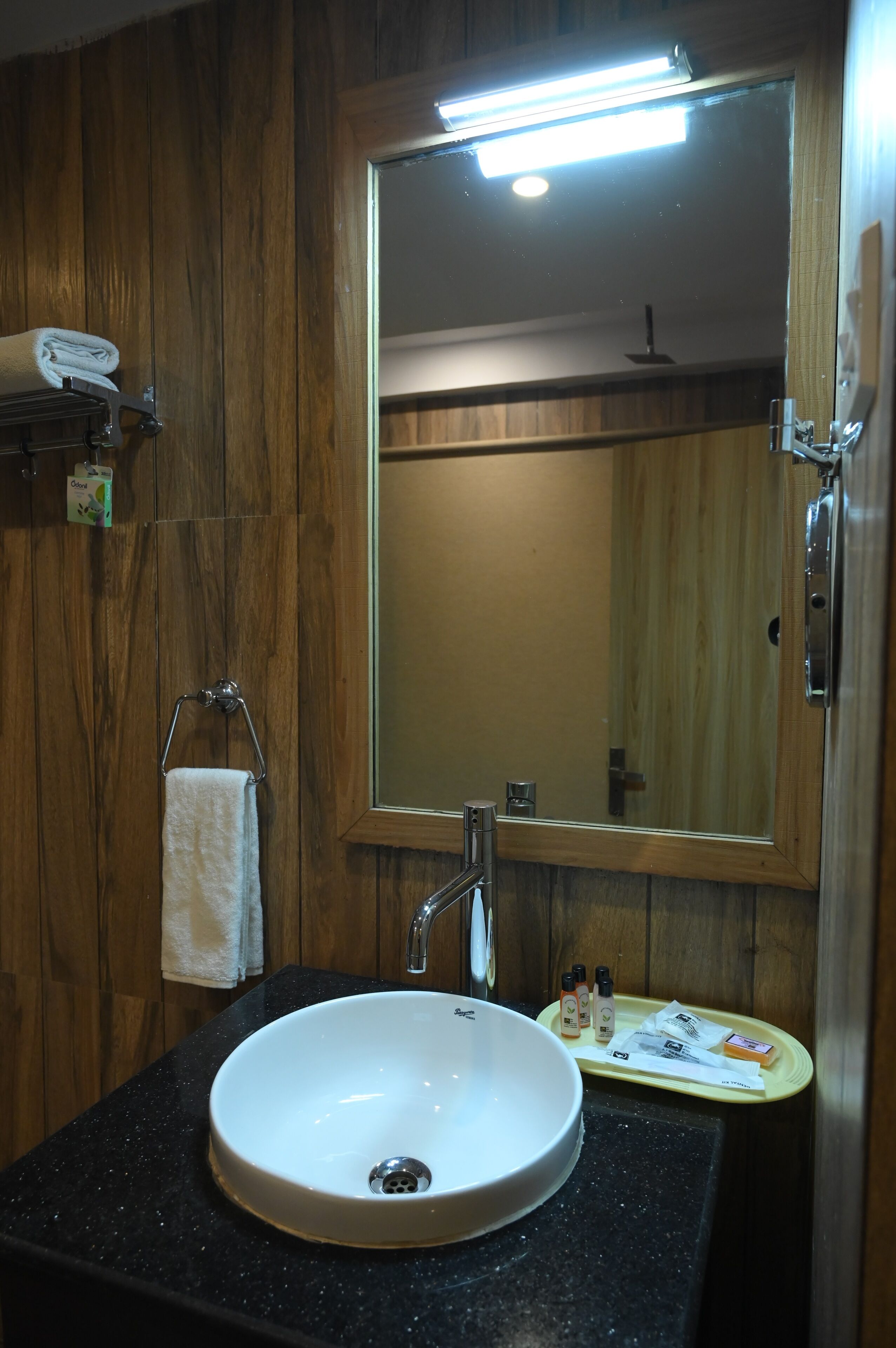 Un baño con pared de madera, un lavamanos blanco, un espejo y artículos de aseo sobre una bandeja.