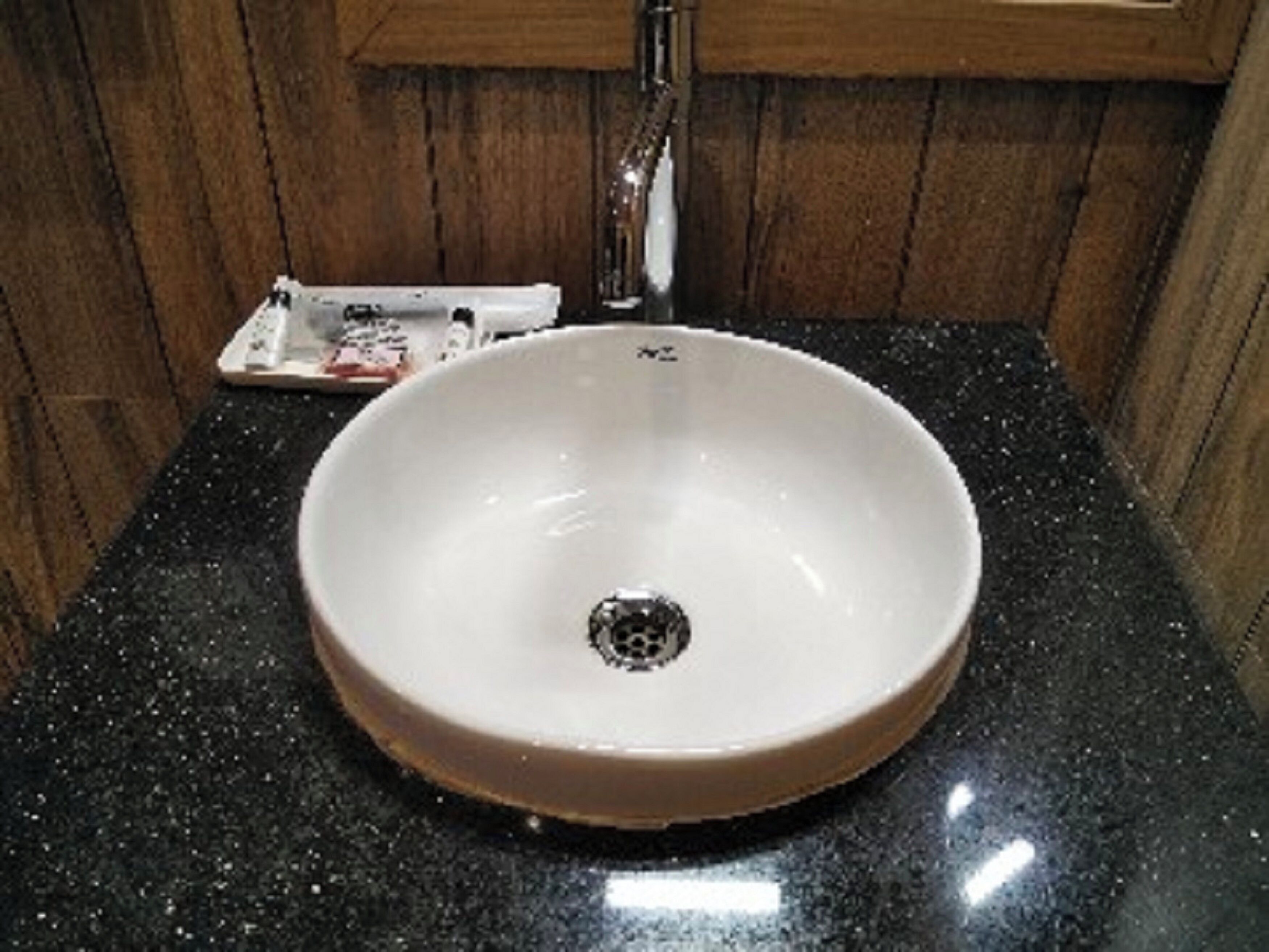 Un lavabo de cerámica blanca con desagüe, sobre una encimera de granito negro en un baño con paneles de madera.