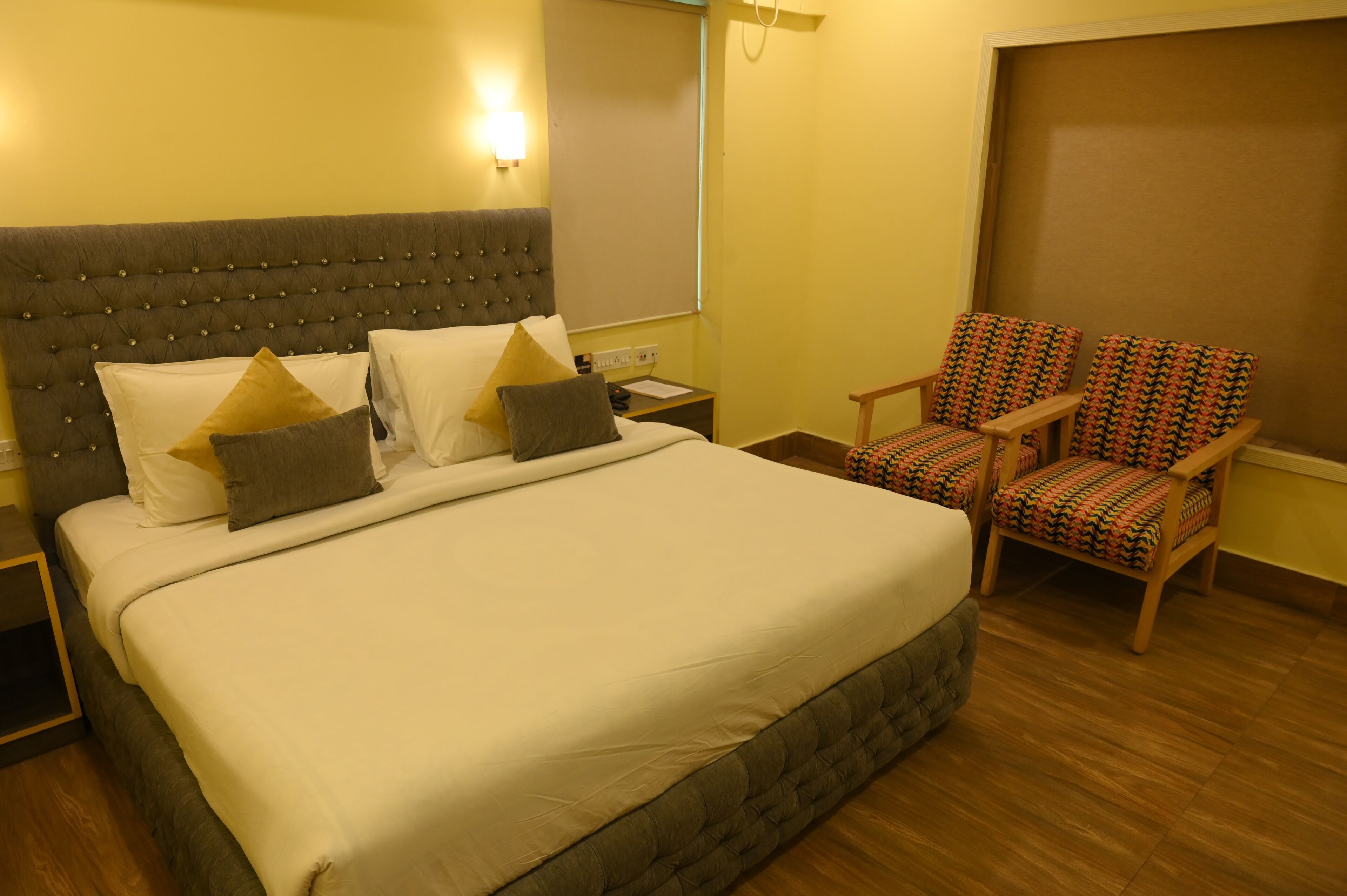 A hotel room with a large bed, two nightstands, a chair, and a window with blinds.