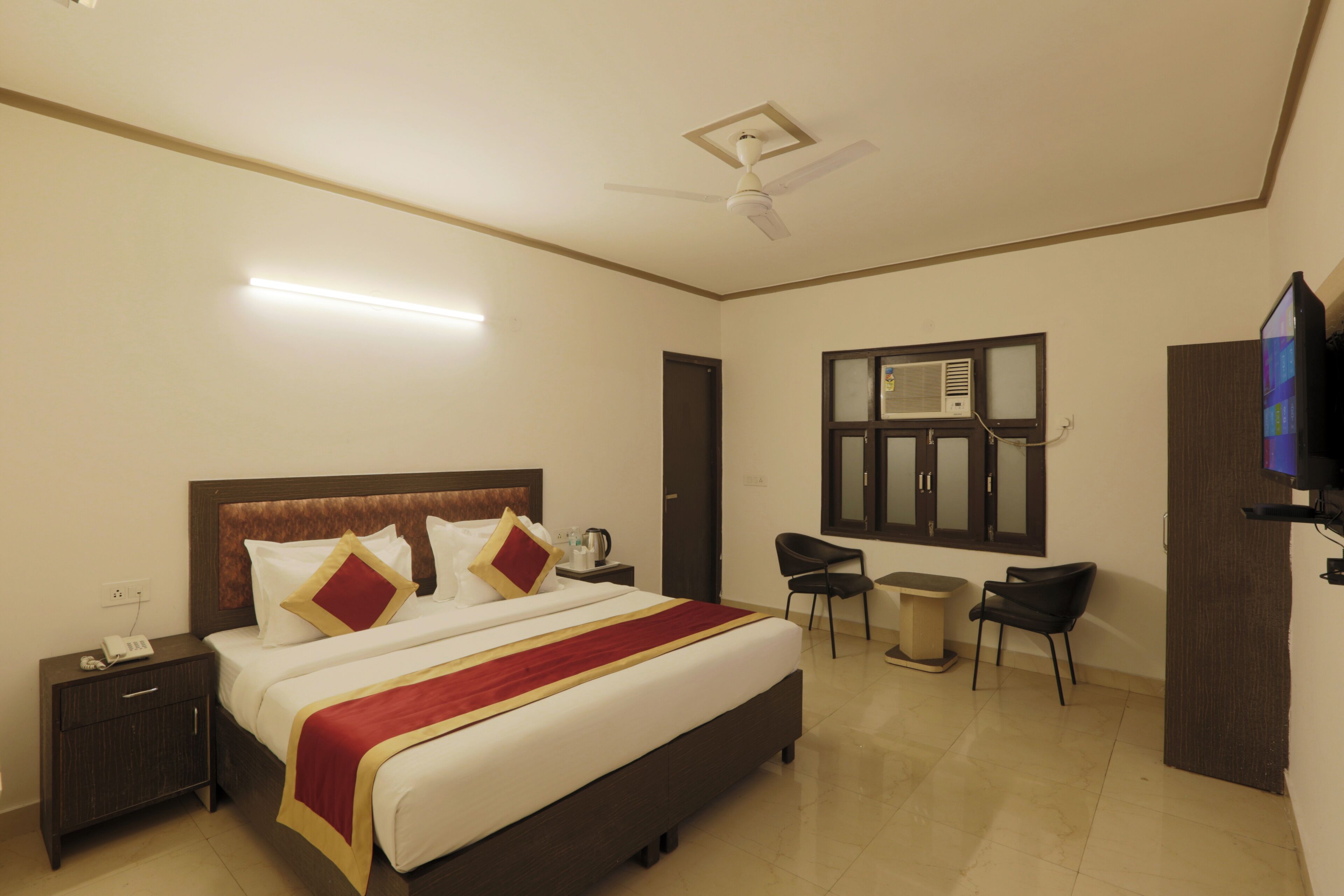 A hotel room with a large bed, bedside tables, a desk, a chair, a television, and a ceiling fan.