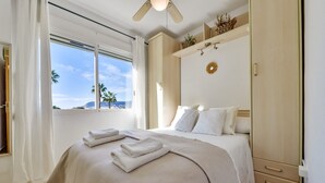 Habitación de hotel con cama, armario, ventilador de techo y vista a palmeras y montañas.