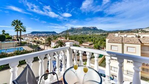 Un balcón con piscina, palmeras y vistas a un pueblo y montañas.