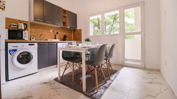 A compact kitchen with a washing machine, a microwave, and a dining area with a table and chairs. - Apartment in the city center (Plovdiv)