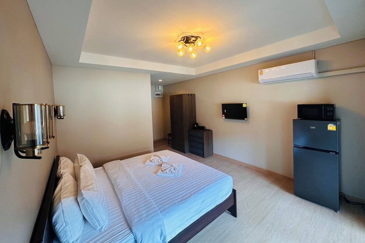 A bedroom with a bed, a flat-screen TV, a refrigerator, and an air conditioning unit.