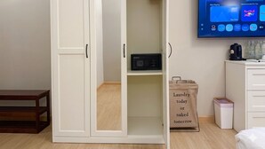 A room with a wardrobe, a television displaying a show, a coffee machine, and a laundry bag. - J STAR (Pattaya)