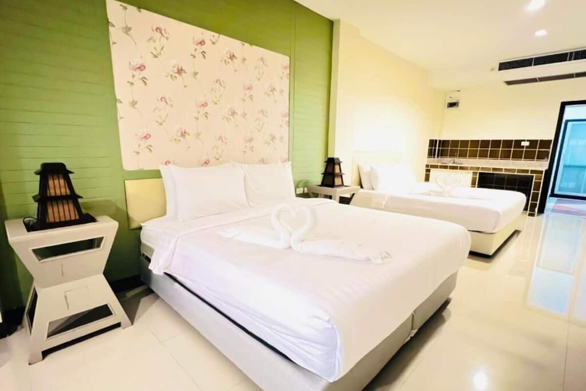 A hotel room with two beds, a green accent wall, a floral headboard, and a modern bathroom visible through the door.