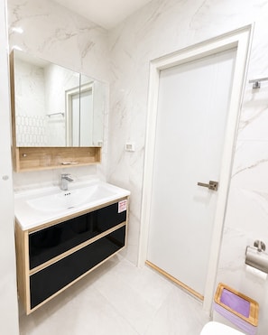 A bathroom with a white marble wall, a white sink with a wooden vanity, a mirror, and a white door.
