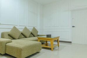 A room with a sofa and a small table, a door, and a white wall with paneling. - J STAR (Pattaya)