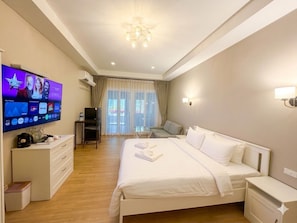 A hotel room with a large bed, a television, a desk, and a chair.