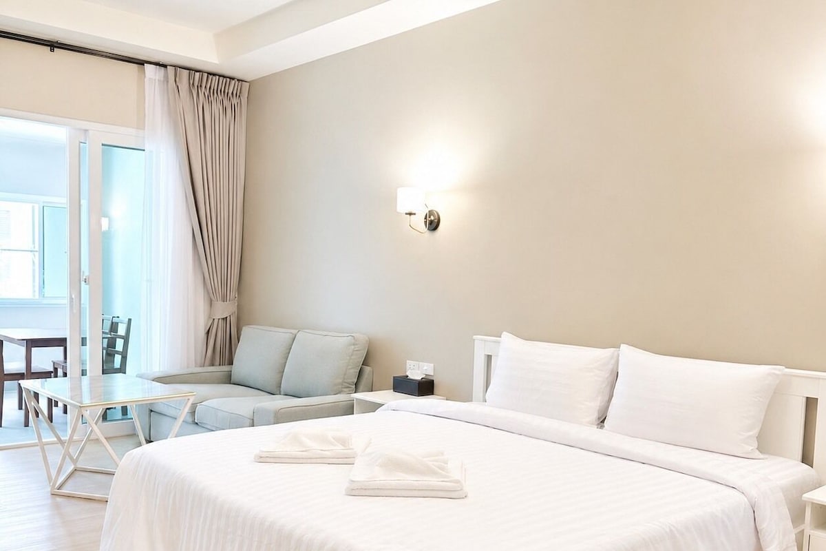 A modern hotel room with a large bed, a small table, a sofa, and a view of the outdoors.