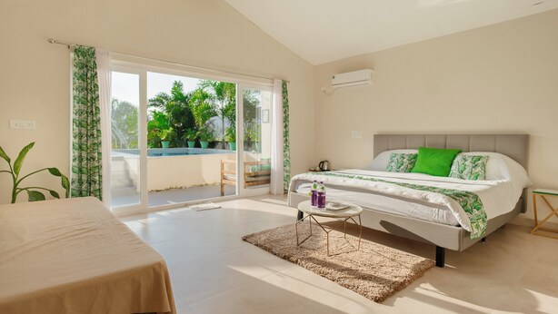 Un dormitorio con cama, mesa, banco y vistas al verdor exterior.