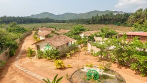 Un pueblo rural con casas tradicionales, un sendero de tierra y un jardín circular verde con una rueda decorativa.