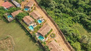 Vista aérea de un complejo turístico con varias construcciones tipo bungaló, cada una con piscina y rodeada de exuberante vegetación.
