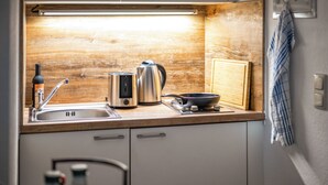 A kitchen with a wooden countertop, a sink, a kettle, a toaster, and a cutting board.