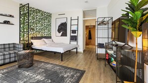 A modern bedroom with a bed, a sofa, a small round table, a plant, and a wardrobe with a hanging rack.