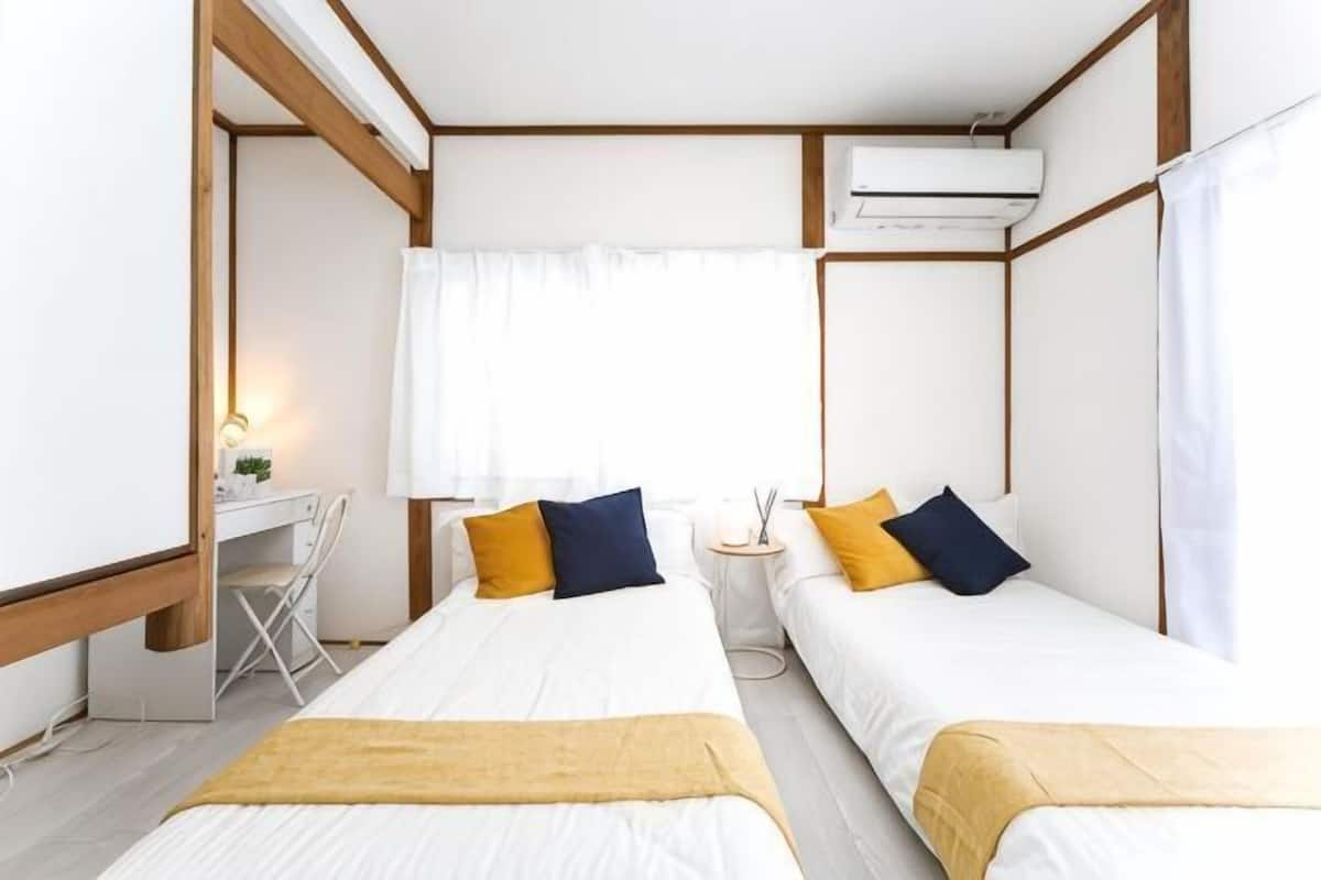 A room with two beds, a desk, and an air conditioning unit.