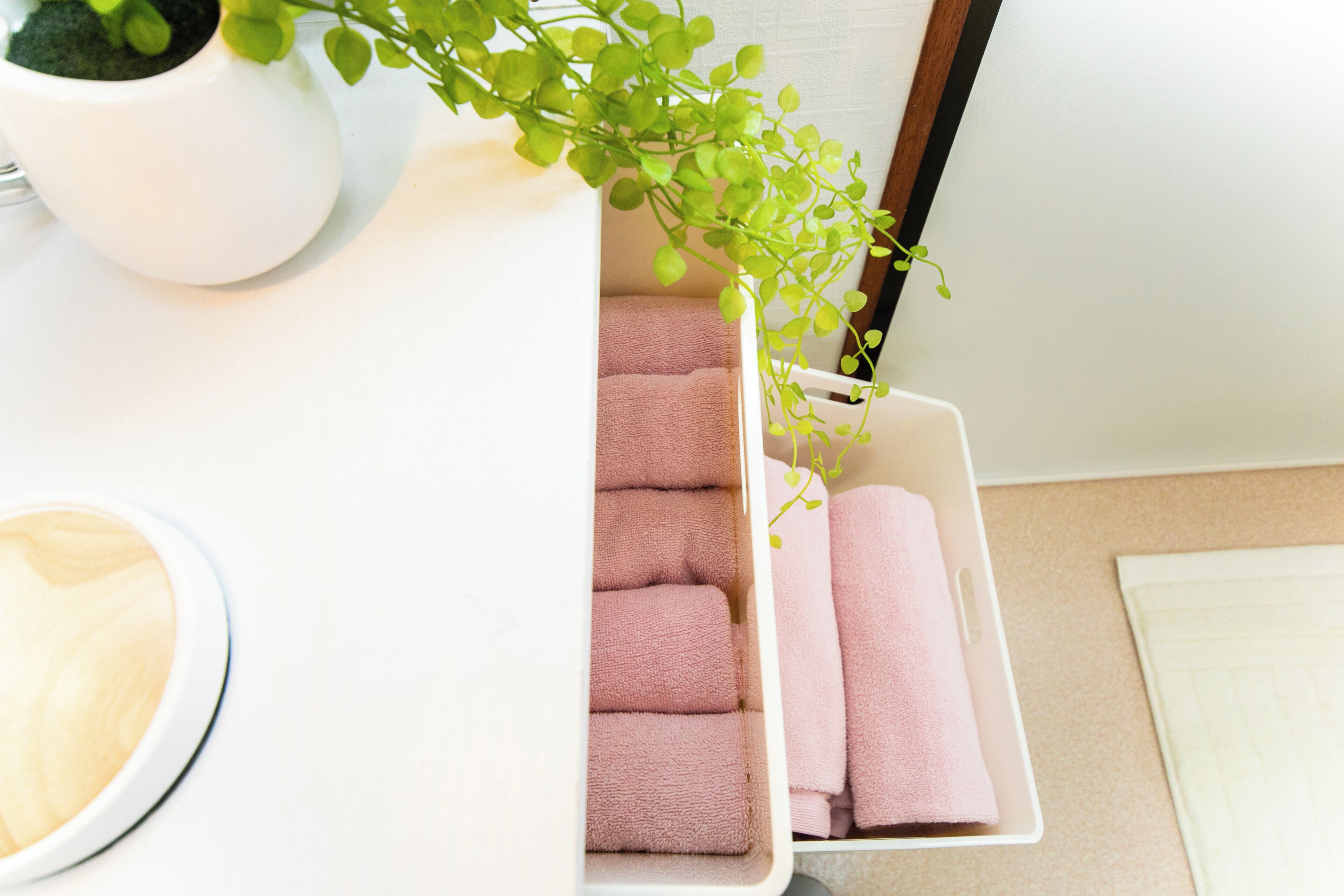 A white storage box with pink towels and a small potted plant.