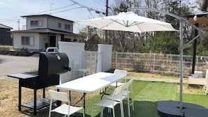 Eine Terrass mit Grill, Tisch, Stühlen und Sonnenschirm.