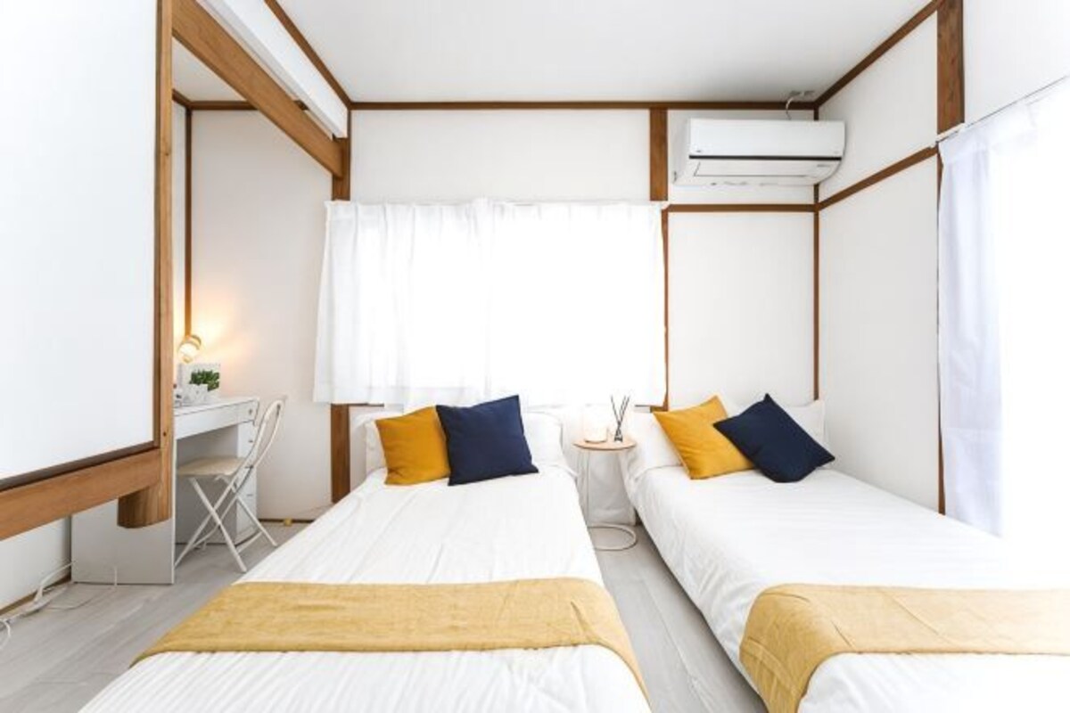 A room with two beds, a desk, and an air conditioning unit.