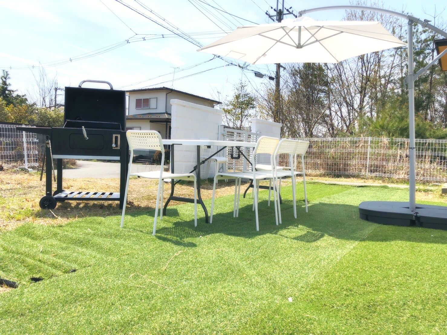 Un patio con una parrilla, sillas blancas y una mesa bajo un paraguas blanco.
