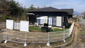 Ein kleines, eingeschossiges Mobilheim mit umzäunter Garten, einer Terrasse und Gartenmöbeln sowie einer Satellitenschüssel.