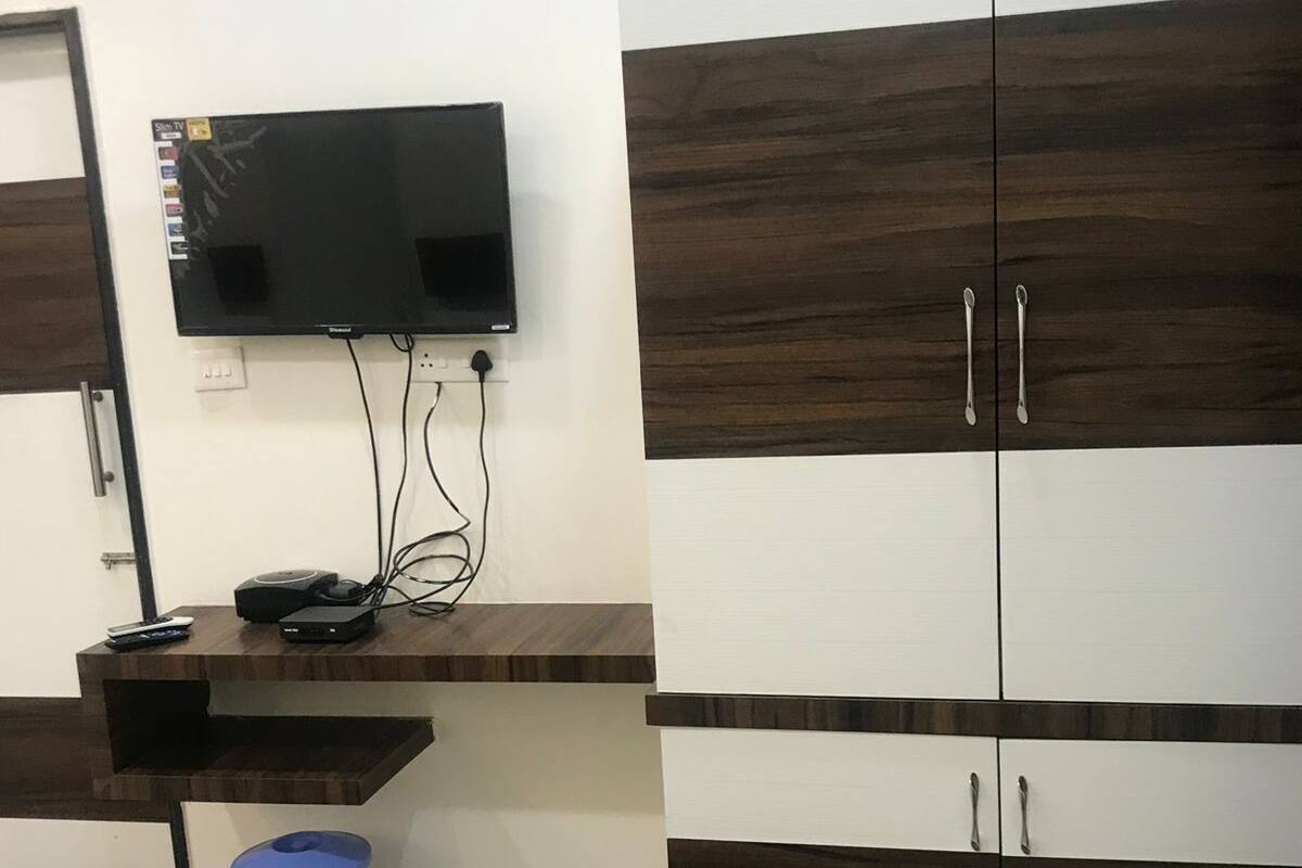 Un dormitori amb un llit, un televisor muntat a la paret, una taula de treball amb un ordinador i un safataire, i un armari amb dues portes.