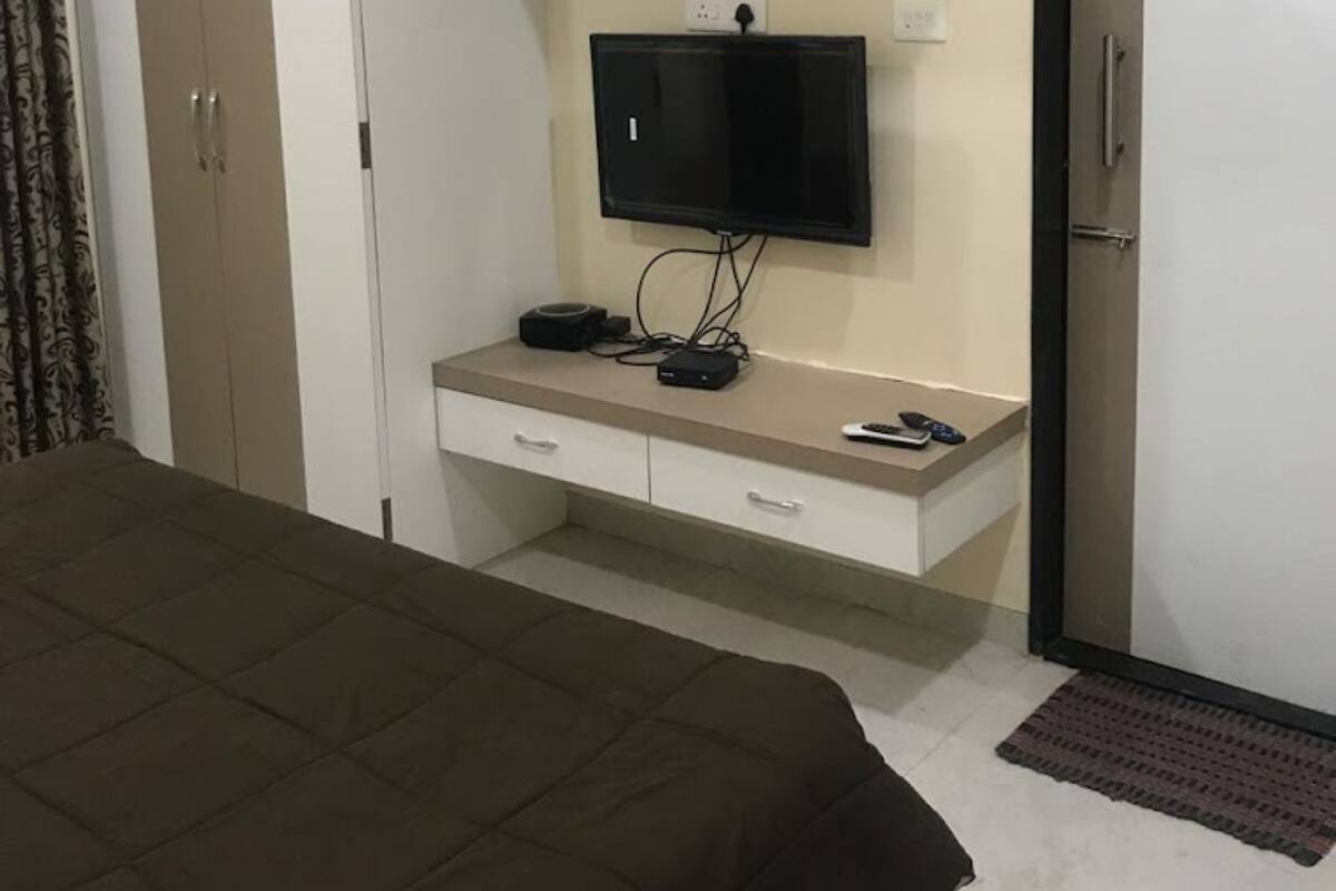 Un dormitori amb un llit, un televisor sobre un suport, un armari i un aparell d'aire condicionat.