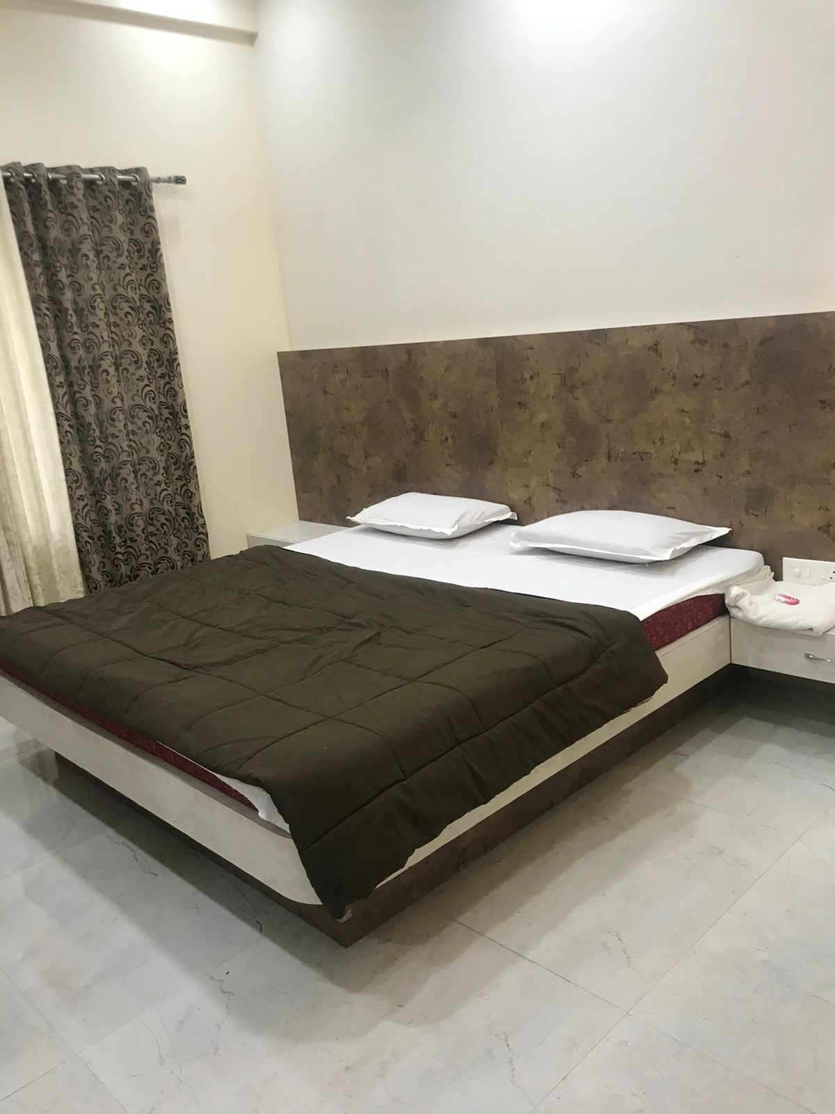 A bed with a brown quilt, white pillows, and a headboard with a textured design.