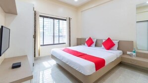 Een hotelkamer met een bed, een televisie, een nachtkastje en een raam met gordijnen.