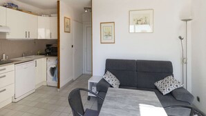 Ein kompakter Wohnbereich mit Küchenzeile, Essbereich und einer Couch mit gemusterten Kissen.