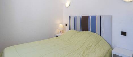 Un lit avec une tête de lit à rayures, une table de chevet avec une lampe et une petite table de nuit blanche.