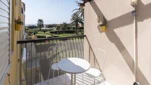 Ein Balkon mit weißem Tisch und Stühlen, der einen angelegten Garten mit Palmen und Meerblick bietet.