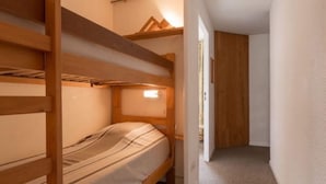 Une chambre avec un lit superposé, une tête de lit en bois, un lit simple et une petite étagère au-dessus du lit.