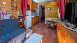 Una habitación acogedora estilo cabaña con interior de madera, una kitchenette, comedor y sala de estar con sofá y televisor.