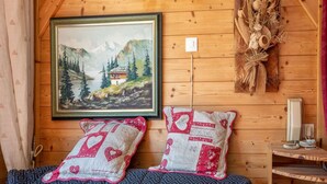 Interior acogedor de una cabaña con un cuadro enmarcados de un paisaje montañoso, dos almohadones estampados, un adorno rústico en la pared y una pequeña mesa con una lámpara.