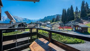 Una terraza de madera con vistas a un pueblo de montaña, que incluye casas y un telesilla.